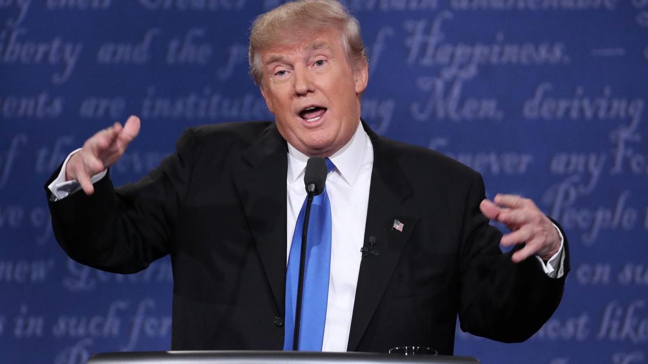 Trump redet und gestikuliert vor dem blauen Hintergrund eines Fernsehstudios. Trump redet und gestikuliert vor dem blauen Hintergrund eines Fernsehstudios.