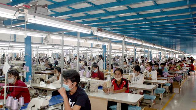 Kambodschanische Arbeiterinnen und Arbeiter sitzen im Jahr 2007 in einer Textilfabrik am Rande Phnom Penhs mit Mundschutz an Nähmaschinen.
