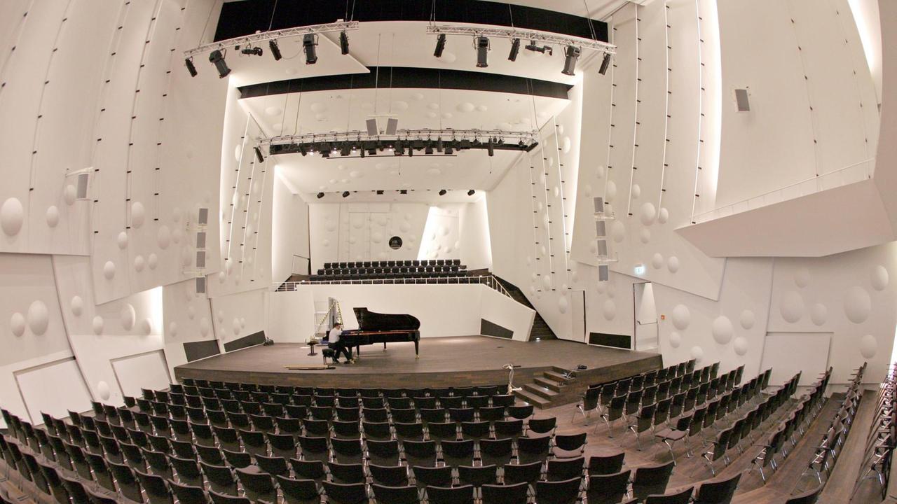 Auf der Bühne im neuen, in Weiß gehaltenen, leeren Konzertsaal der Musikhochschule in Dresden sitzt ein Mann an einem großen Konzertflügel. Auf der Bühne im neuen, in Weiß gehaltenen, leeren Konzertsaal der Musikhochschule in Dresden sitzt ein Mann an einem großen Konzertflügel.