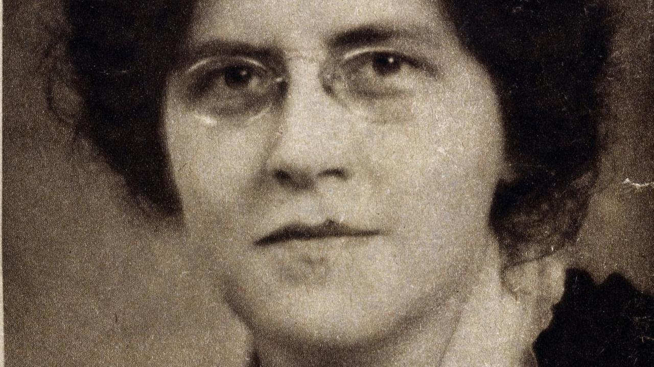 Porträt einer Frau mit Brille und leicht zurückgesteckten Haaren, die in die Kamera lächelt. Porträt einer Frau mit Brille und leicht zurückgesteckten Haaren, die in die Kamera lächelt.