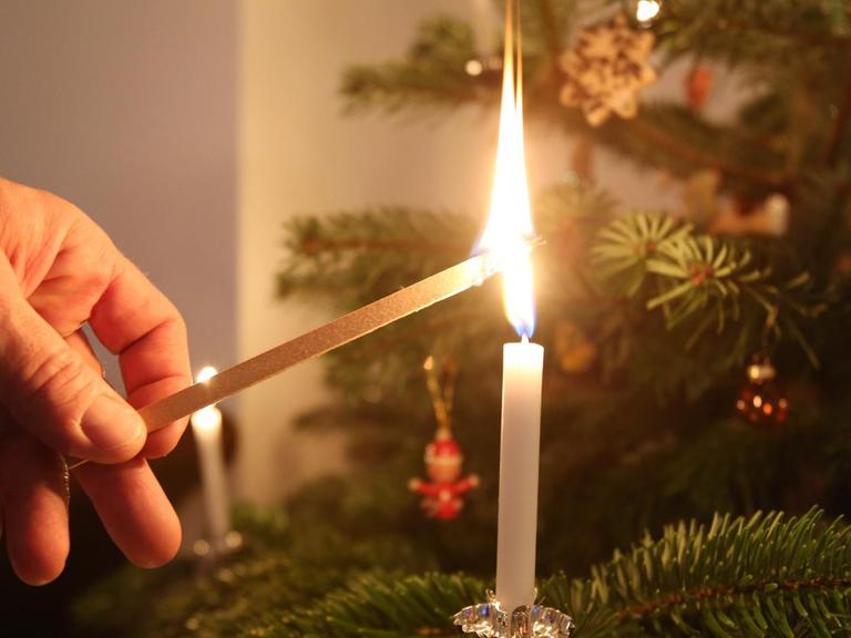 Mit einem großen Streichholz zündet ein Mann eine Kerze an einem Weihnachtsbaum in Hamburg an