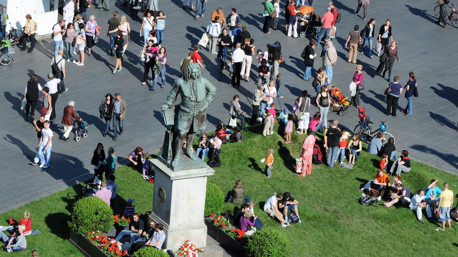 Zahlreiche Menschen sitzen im Stadtzentrum in Halle/Saale auf einer Wiese, die aus Anlass der Händelfestspiele rund um das Händeldenkmal ausgelegt wurde, Juni 2014