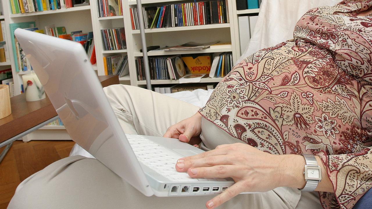 Eine schwangere Frau sitzt mit einem Laptop auf dem Sofa. Eine schwangere Frau sitzt mit einem Laptop auf dem Sofa.