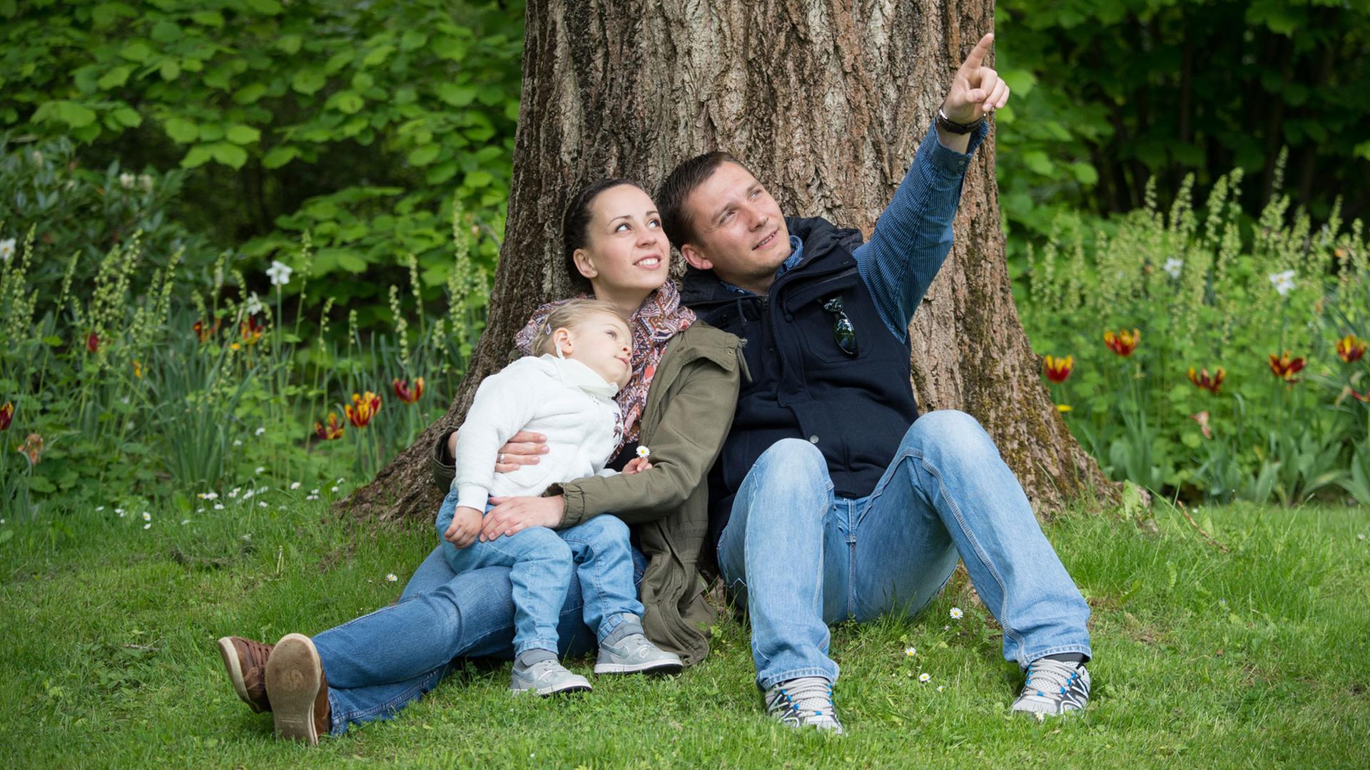 Ein junges Paar mit Kind sitzt auf einer Wiese unter einem Baum. Ein junges Paar mit Kind sitzt auf einer Wiese unter einem Baum.