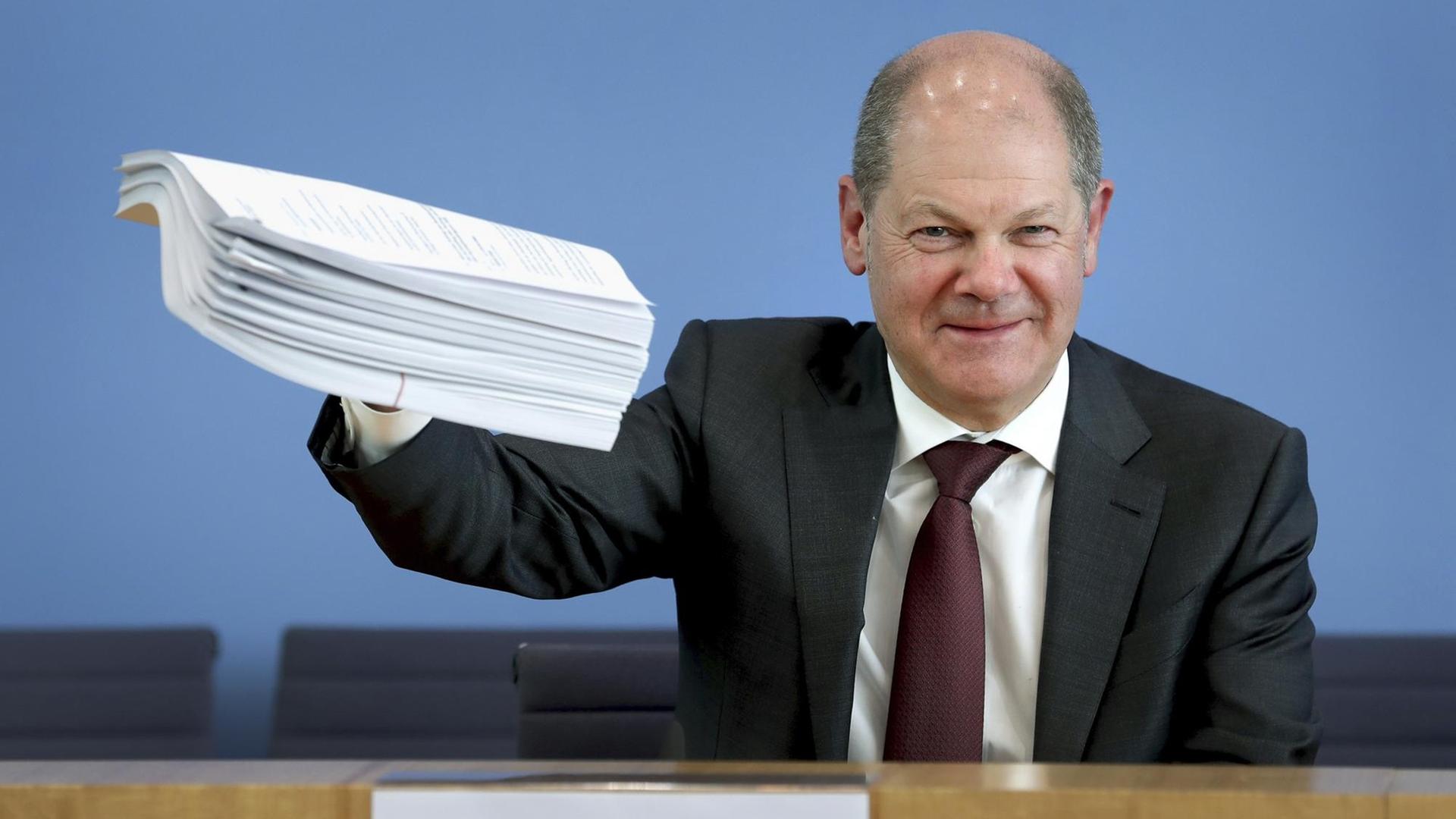 Olaf Scholz (SPD), Bundesfinanzminister, gibt eine Pressekonferenz zum Hilfspaket der Bundesregierung für Betroffene der Corona-Krise und hält einen Stapel Unterlagen in die Höhe. Olaf Scholz (SPD), Bundesfinanzminister, gibt eine Pressekonferenz zum Hilfspaket der Bundesregierung für Betroffene der Corona-Krise und hält einen Stapel Unterlagen in die Höhe.