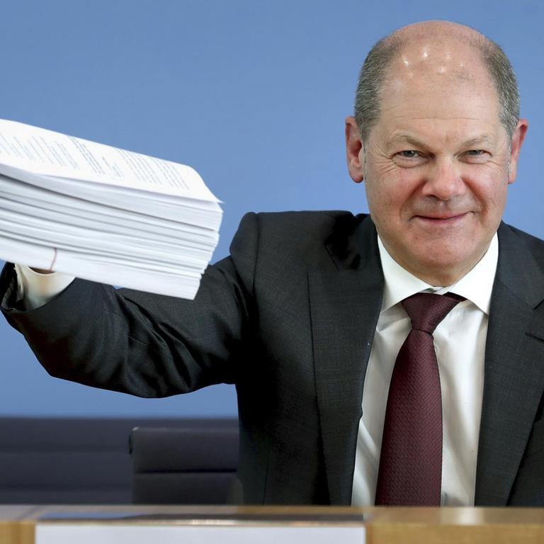 Olaf Scholz (SPD), Bundesfinanzminister, gibt eine Pressekonferenz zum Hilfspaket der Bundesregierung für Betroffene der Corona-Krise und hält einen Stapel Unterlagen in die Höhe.