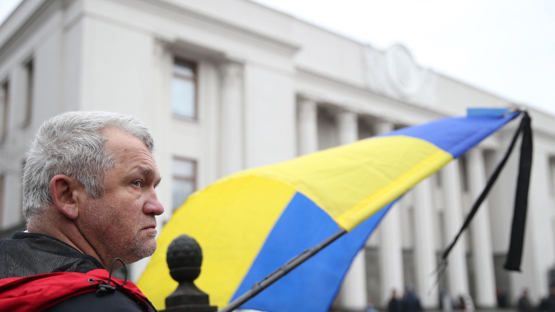 Ein Mann mit einer Ukraine-Flagge wartet vor dem Parlament in Kiew. Ein Mann mit einer Ukraine-Flagge wartet vor dem Parlament in Kiew.