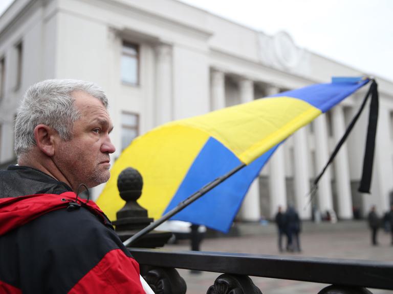 Ein Mann mit einer Ukraine-Flagge wartet vor dem Parlament in Kiew.