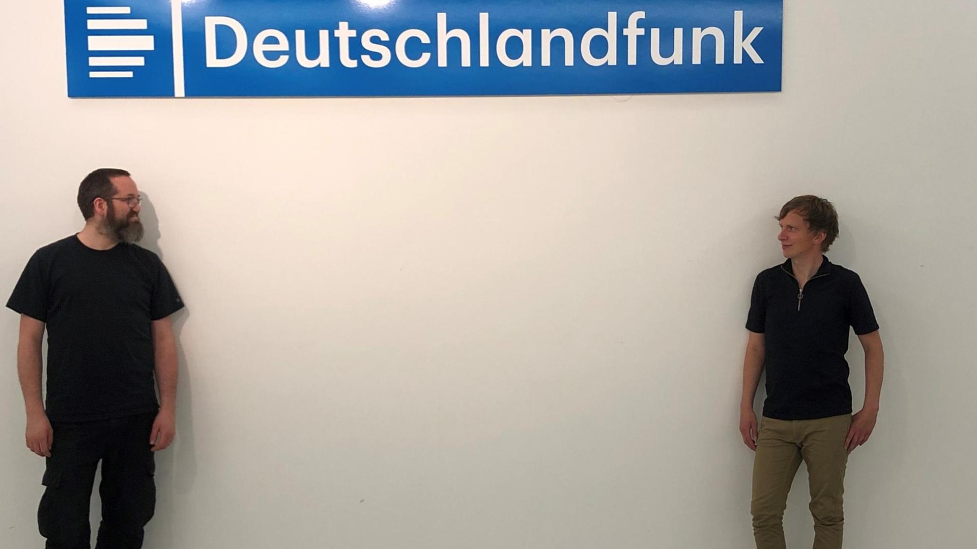 Unter dem Deutschlandfunk Logo stehen sich zwei Männer auf Abstand gegenüber und schauen sich an.