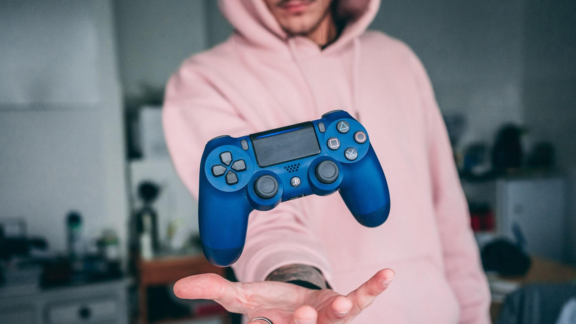 Ein junger Mann mit Kapuzenpulli wirft einen Game Controller in die Luft. Ein junger Mann mit Kapuzenpulli wirft einen Game Controller in die Luft.