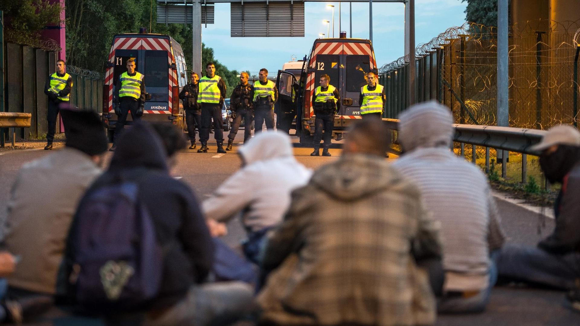 Flüchtlinge sitzen am Eurotunnel in Calais. Der Weg wird von Polizisten blockiert. Flüchtlinge sitzen am Eurotunnel in Calais. Der Weg wird von Polizisten blockiert.