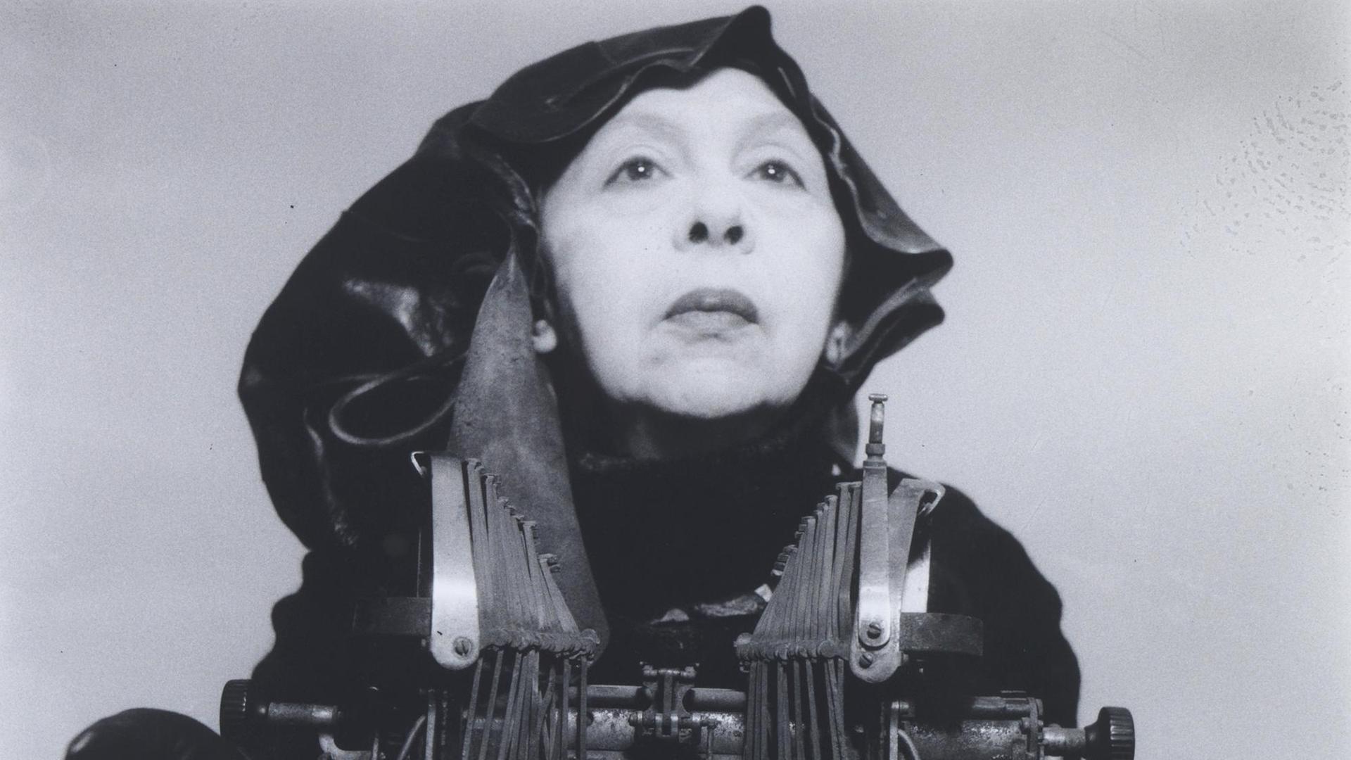 Das Kunstwerk "Mrs Oliver in her traveling costume" von Geta Brătescu. Ein Schwarz-Weiss-Foto das die in ganz in schwarz gekleidete Künstlerin mit einer mechanischen Schreibmaschine zeigt. Das Kunstwerk "Mrs Oliver in her traveling costume" von Geta Brătescu. Ein Schwarz-Weiss-Foto das die in ganz in schwarz gekleidete Künstlerin mit einer mechanischen Schreibmaschine zeigt.
