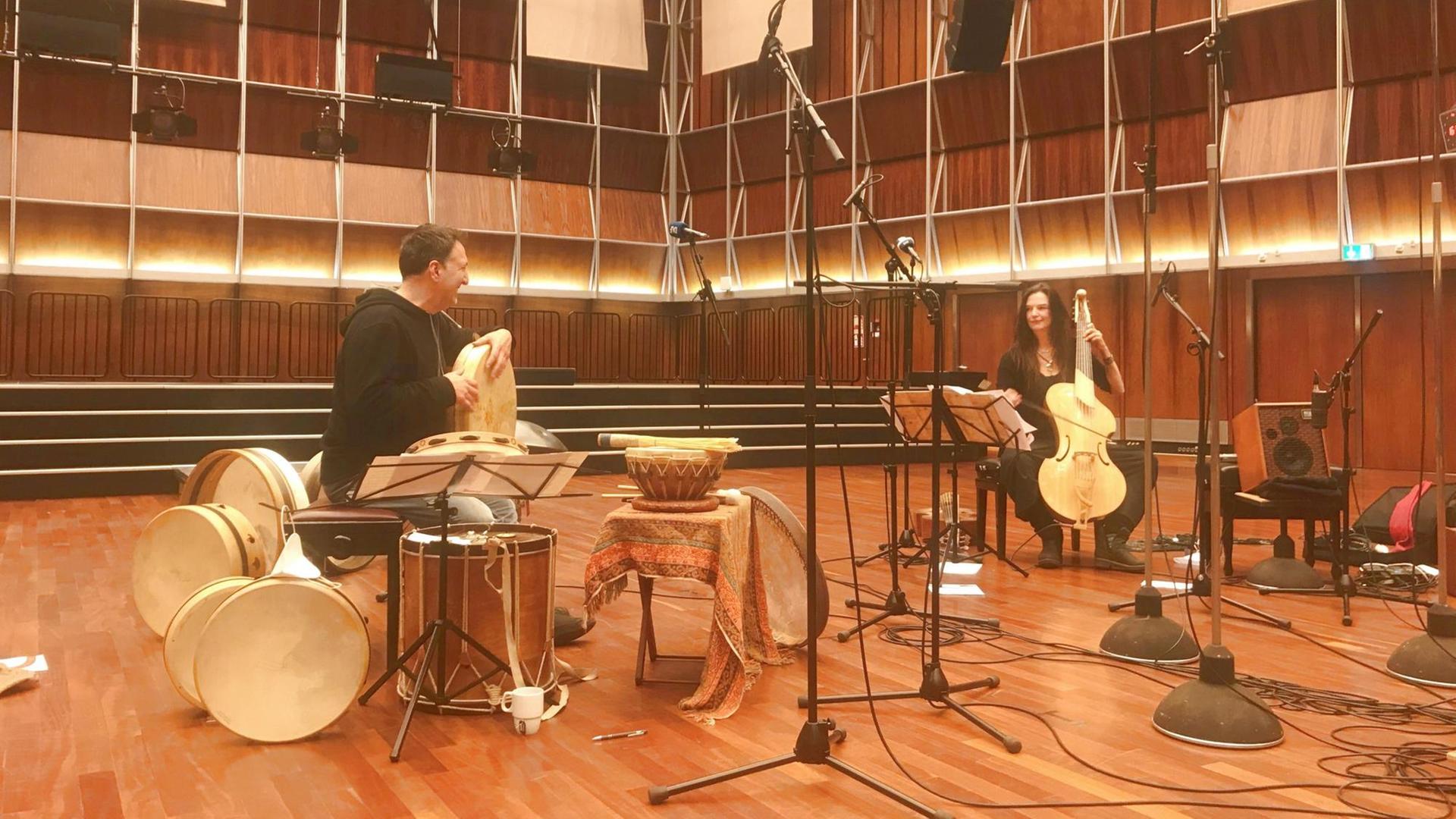 Aufnahme aus dem Deutschlandfunk Kammermusiksaal. Auf der linken Seite sitzt der Perkussionist mit vielen Schlaginstrumenten und Trommeln um sich herum, er hält eine Rahmentrommel in den Händen, trägt ein schwarzes Kapuzenshirt und schaut zur Gambistin auf der rechten Seite. Sie spielt eine elektrisch verstärkte Gambe, im holzgetäfelten Saal sind viele Mikrofone aufgestellt. Aufnahme aus dem Deutschlandfunk Kammermusiksaal. Auf der linken Seite sitzt der Perkussionist mit vielen Schlaginstrumenten und Trommeln um sich herum, er hält eine Rahmentrommel in den Händen, trägt ein schwarzes Kapuzenshirt und schaut zur Gambistin auf der rechten Seite. Sie spielt eine elektrisch verstärkte Gambe, im holzgetäfelten Saal sind viele Mikrofone aufgestellt.