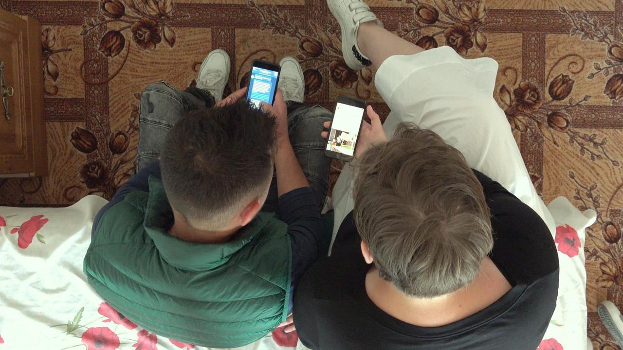 Film-Still aus "Welcome to Chechnya": Zwei Männer sitzen mit Smartphones nebeneinander. Film-Still aus "Welcome to Chechnya": Zwei Männer sitzen mit Smartphones nebeneinander.