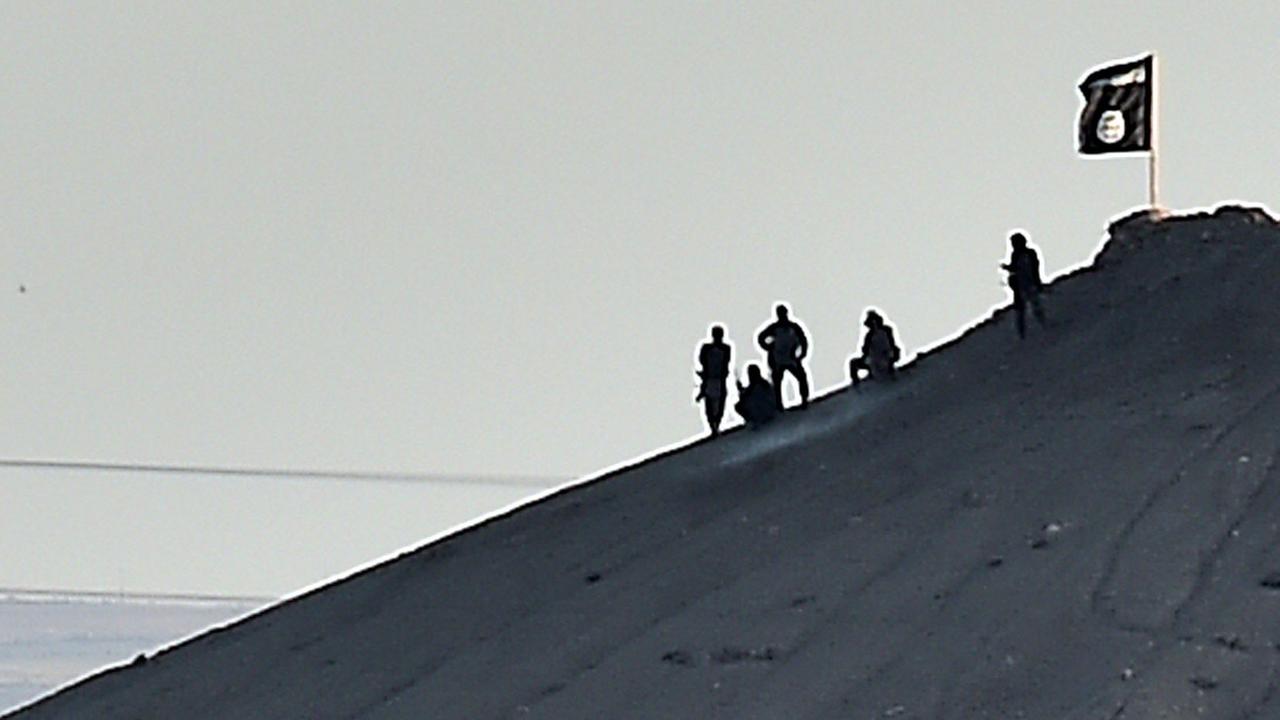 Mutmaßliche Kämpfer des Islamischen Staates hissen die Flagge der Miliz auf einem Hügel bei Kobane in Syrien. Mutmaßliche Kämpfer des Islamischen Staates hissen die Flagge der Miliz auf einem Hügel bei Kobane in Syrien.