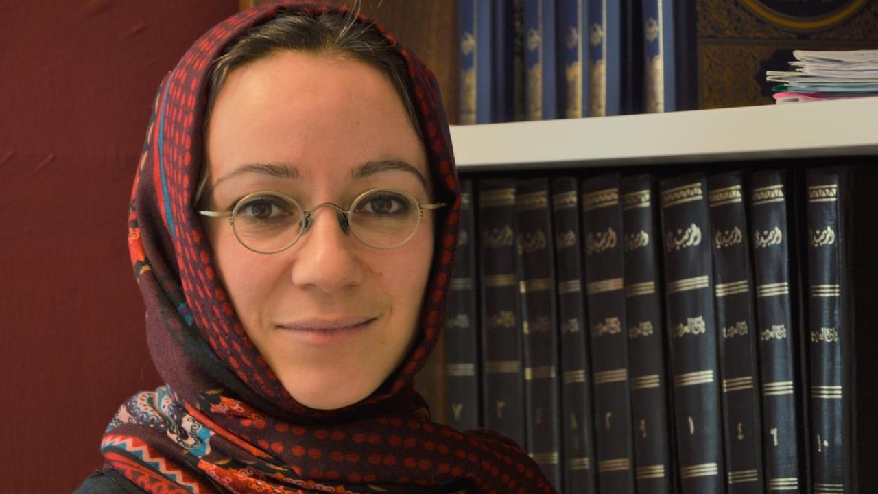 Muna Tatari neben einem Regal mit arabischen Büchern. 
