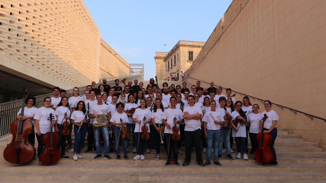 Ein Orchester mit jungen Menschen hat sich auf einer großen Treppe aufgestellt.