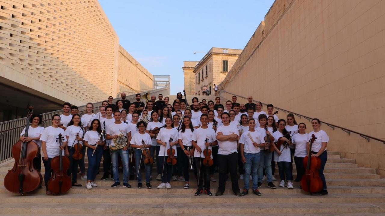 Ein Orchester mit jungen Menschen hat sich auf einer großen Treppe aufgestellt. Ein Orchester mit jungen Menschen hat sich auf einer großen Treppe aufgestellt.