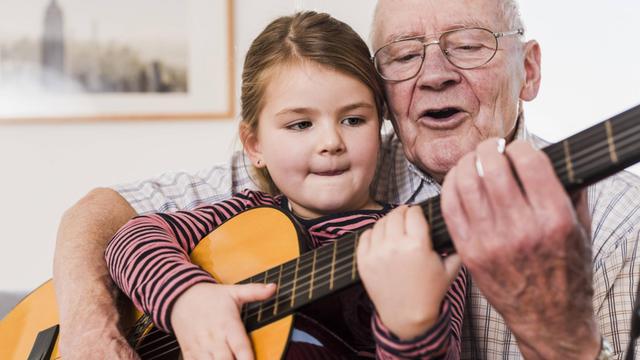 Ein Großvater spielt Gitarre und singt, während seine Enkelin auf seinem Schoß sitzt.