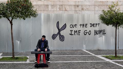 Ein Straßenmusiker am Keyboard vor einem Graffiti: zu sehen eine Schere und der Satz "Cut the dept. IMF go home"