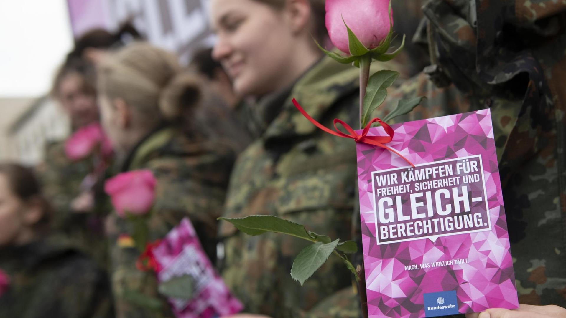 Eine Bundeswehrsoldatin ist schemenhaft hinter einem Flyer zu erkennen, auf dem steht: "Wir kämpfen für Freiheit, Sicherheit und Gleichberechtigung."