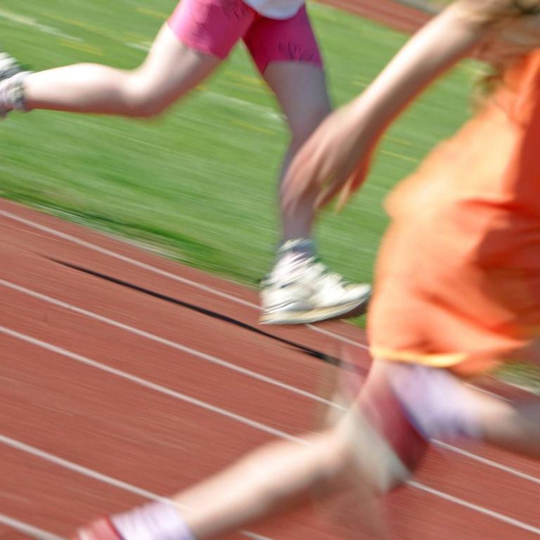 Kinder laufen über eine Laufbahn, zu sehen sind nur die Beine, unscharf.