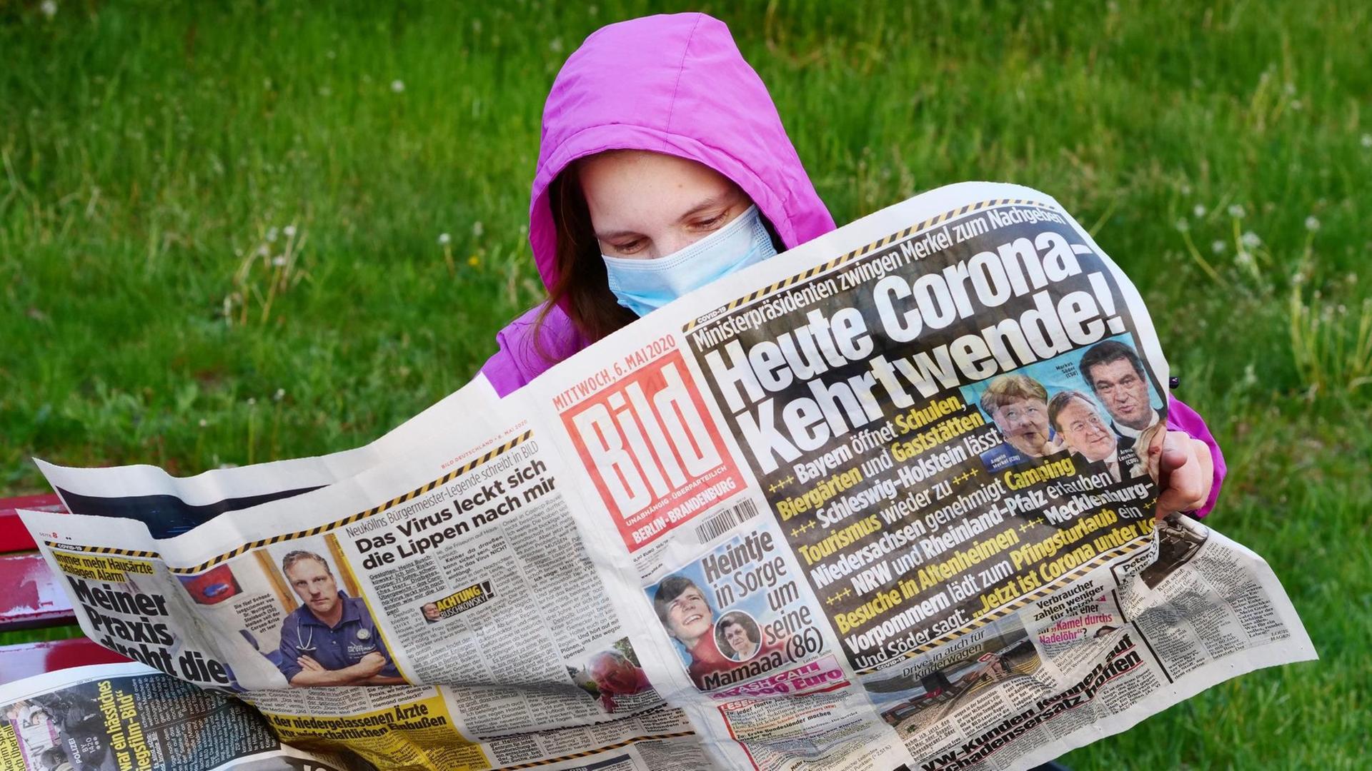 Eine Frau trägt eine Maske zum Schutz gegen das neuartige Coronavirus, während sie auf einer Bank sitzt und die Bildzeitung liest.Die Titelschlagzeile lautet: "Heute Corona-Kehrtwende!". Eine Frau trägt eine Maske zum Schutz gegen das neuartige Coronavirus, während sie auf einer Bank sitzt und die Bildzeitung liest.Die Titelschlagzeile lautet: "Heute Corona-Kehrtwende!".