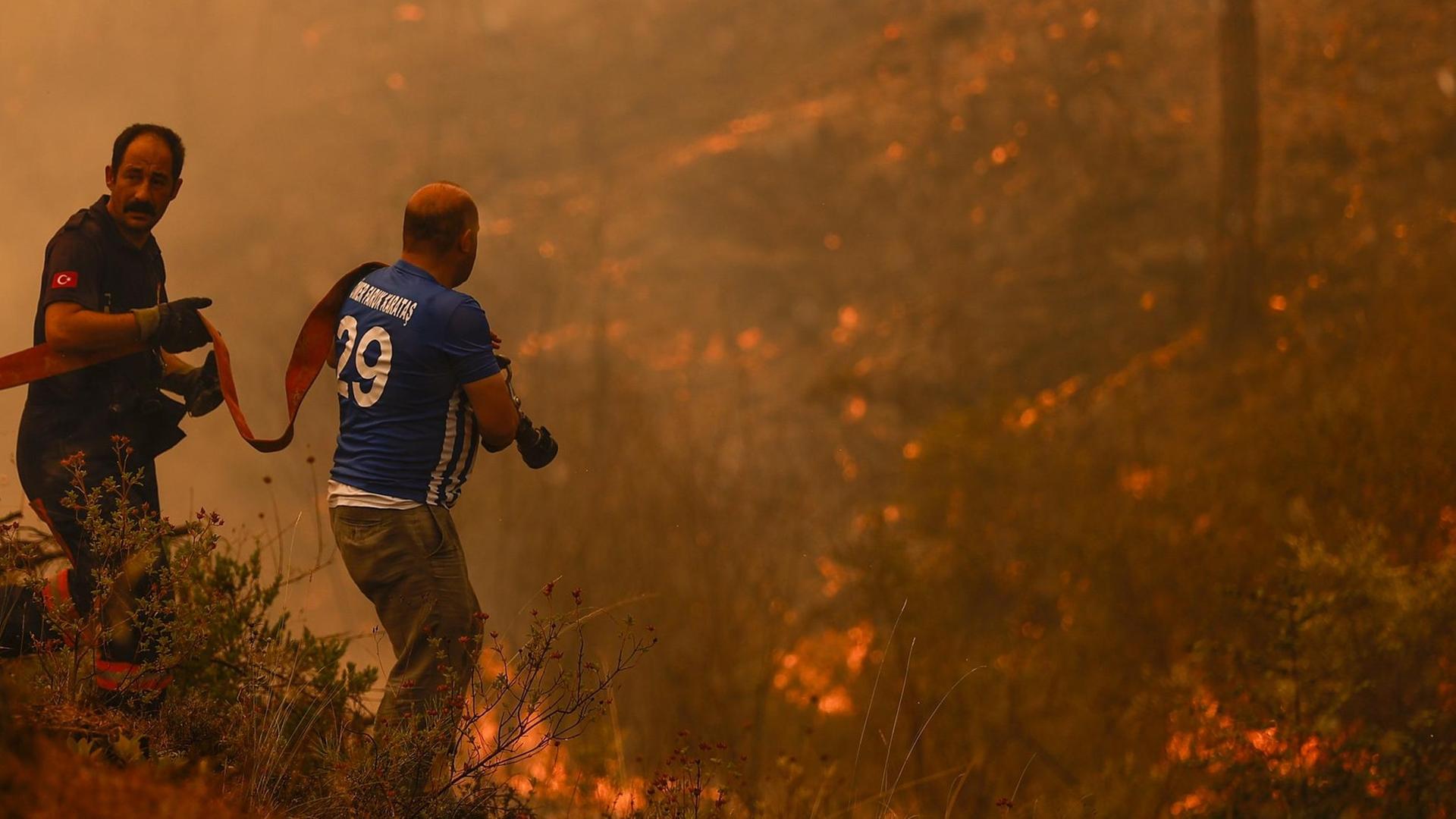 Zwei Männer bringen in der Türkei einen Wasser-Schlauch zu den Wald-Bränden.