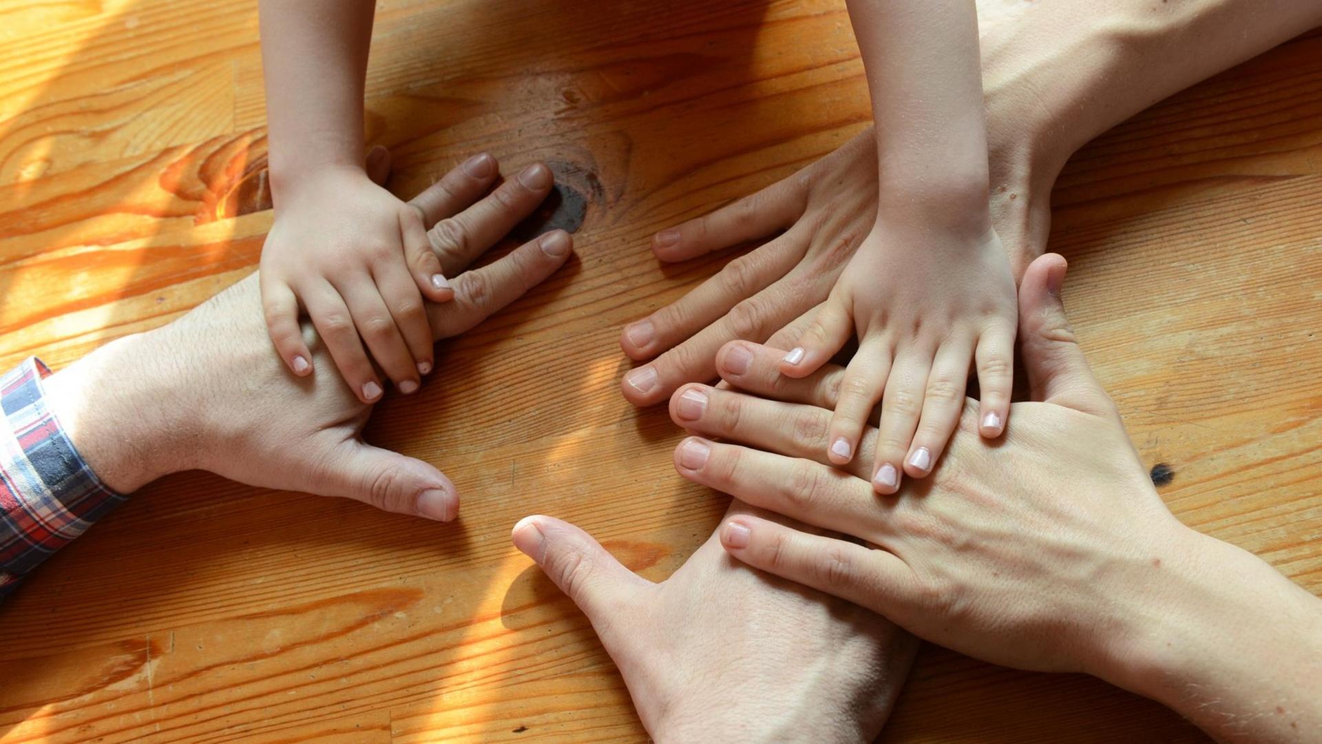 Die Hände eines homosexuellen Paares und eines Kindes liegen auf einem Tisch.