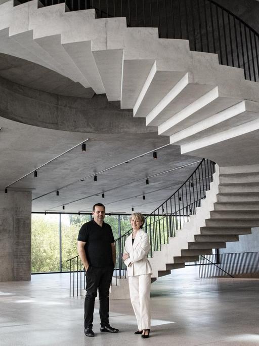 Die beiden stehen in einem Obergeschoß aus Beton, in dessen Mitte eine spektakuläre Wendeltreppe in den Stock darüber ragt.
