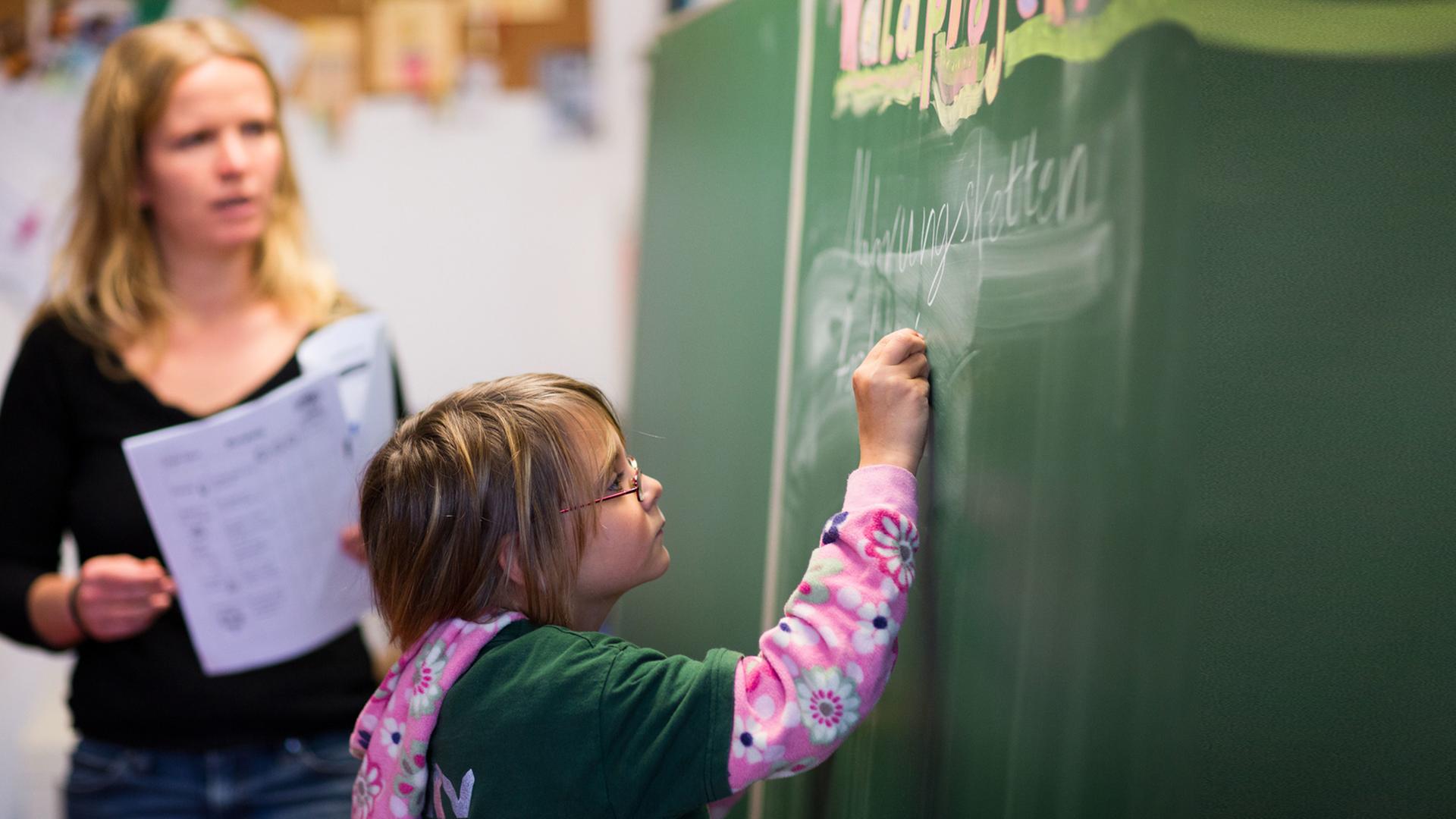 Die neunjährige Cora schreibt, beobachtet von Klassenlehrerin Anne John, in der Freien Schule in Bröbberow an die Schultafel. Die neunjährige Cora schreibt, beobachtet von Klassenlehrerin Anne John, in der Freien Schule in Bröbberow an die Schultafel.