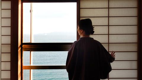 Eine Geisha schaut aus einem Teehaus auf das Meer.