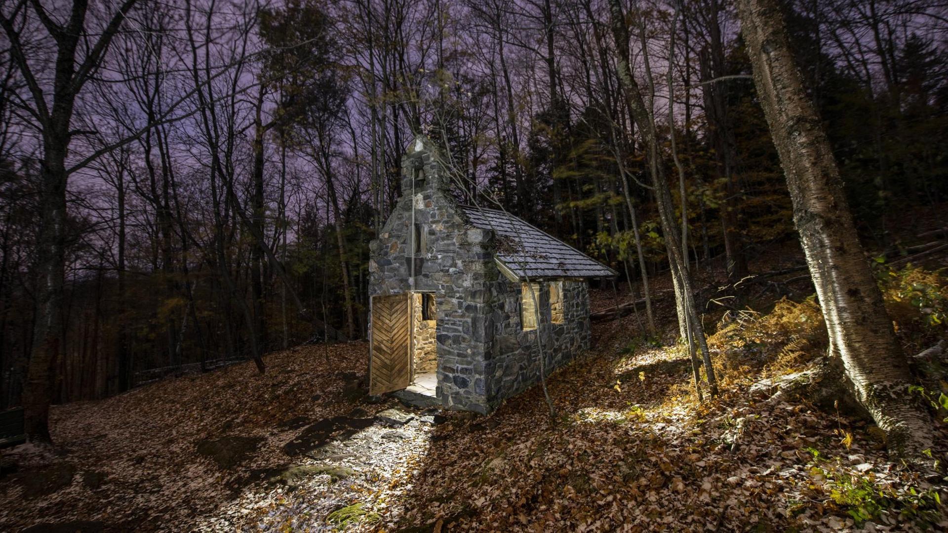 Eine einsame kleine Steinhütte in einem herbstlichen Wald.