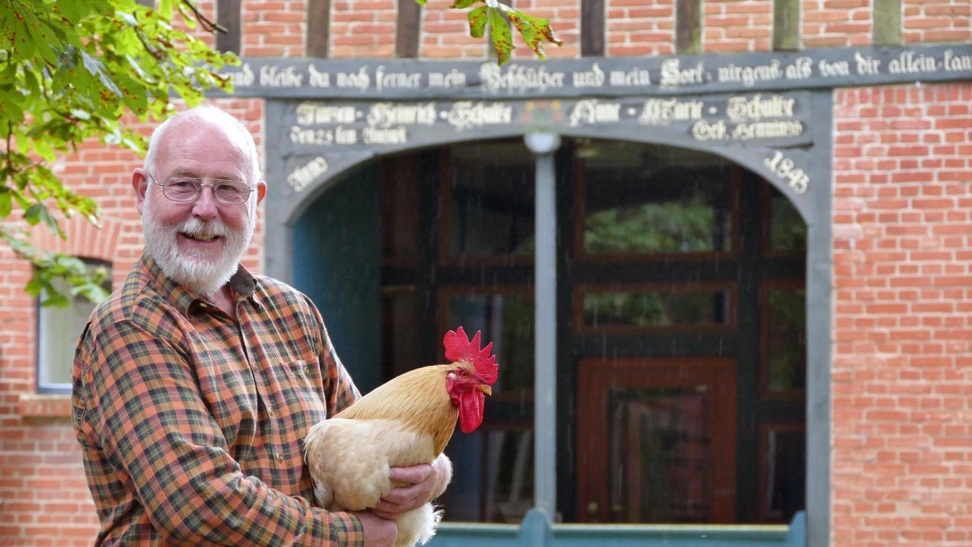Kunst- und Werklehrer Michael Seelig hält einen Hahn in der Hand. Er hat gemeinsam mit seiner Frau den Werkhof Kukate - eine Bildungsstätte für handwerkliche Tätigkeiten -gegründet.