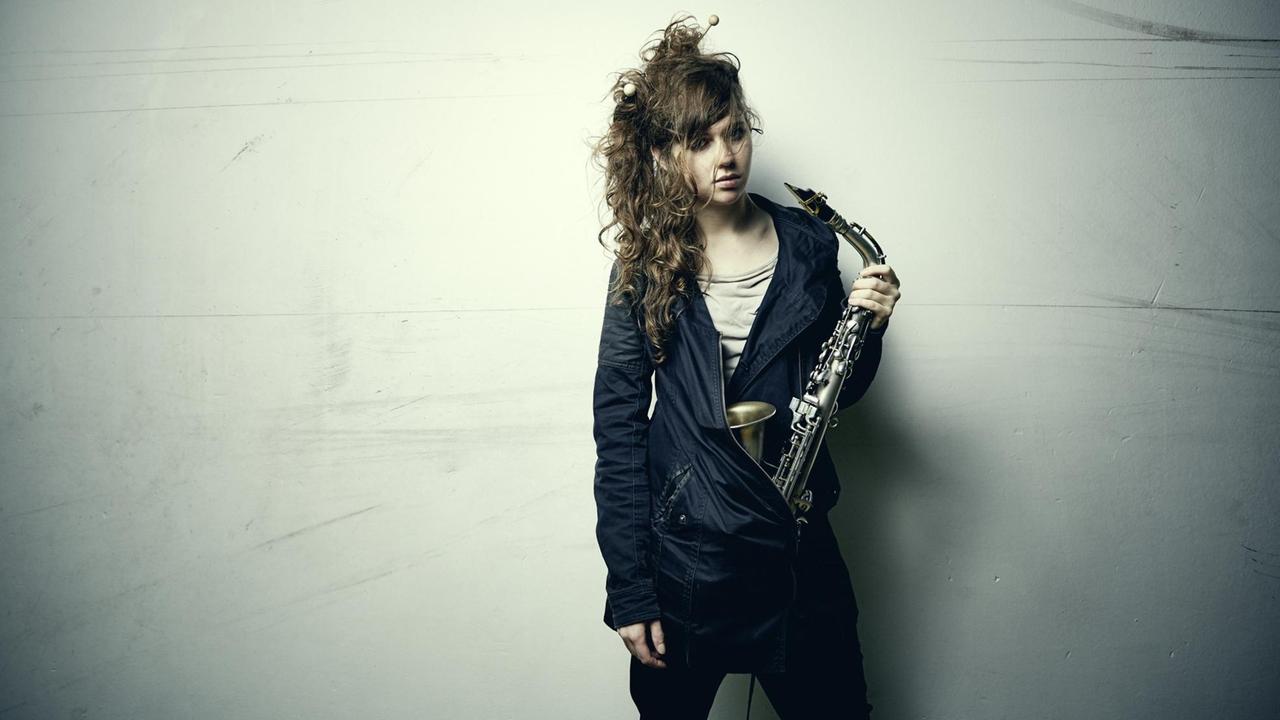 Das Bild zeigt die Jazz-Muisikerin Anna-Lena Schnabel mit einem Saxophin in der linken Hand. Das Bild zeigt die Jazz-Muisikerin Anna-Lena Schnabel mit einem Saxophin in der linken Hand.