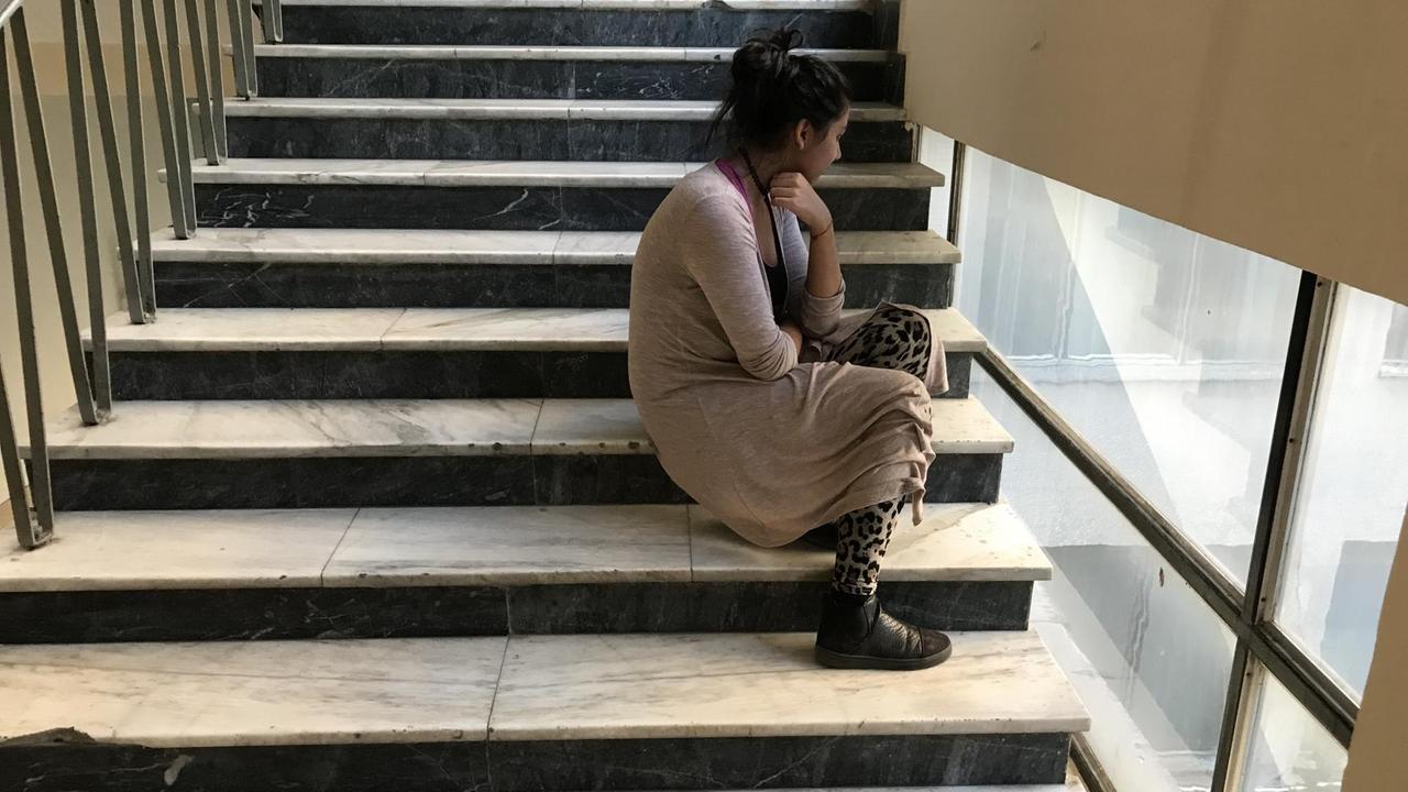 Mädchen lehnt sitzend am Treppengeländer in einer Schule. Mädchen lehnt sitzend am Treppengeländer in einer Schule.