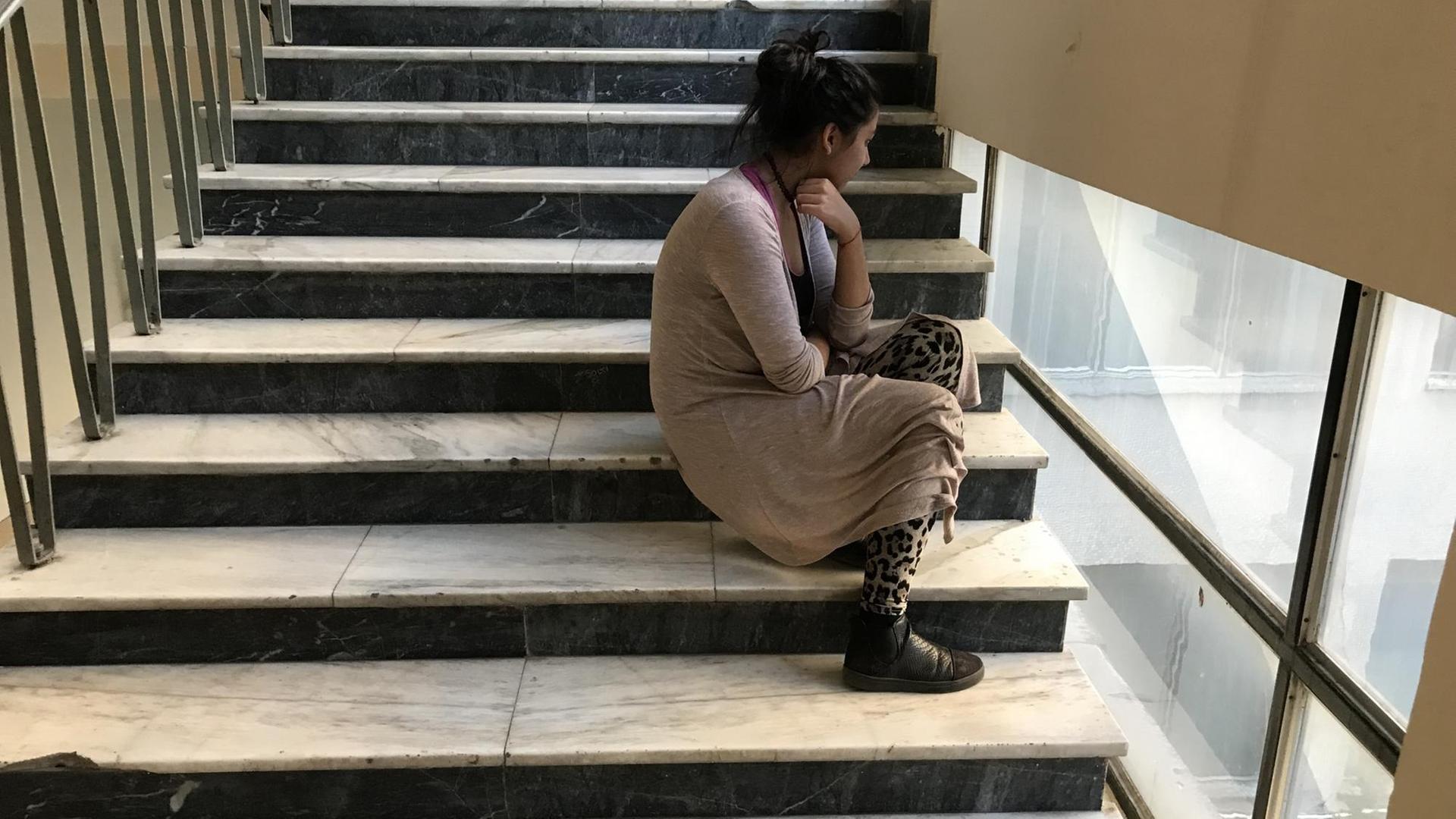 Mädchen lehnt sitzend am Treppengeländer in einer Schule. Mädchen lehnt sitzend am Treppengeländer in einer Schule.