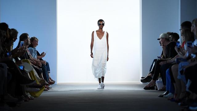 Bei der Modepräsentation des Labels "Hien Le" während der Fashion Week Berlin im Sommer 2017 in Berlin läuft ein Model im schlichten, weißen Kleid auf dem Laufsteg am Publikum vorbei.