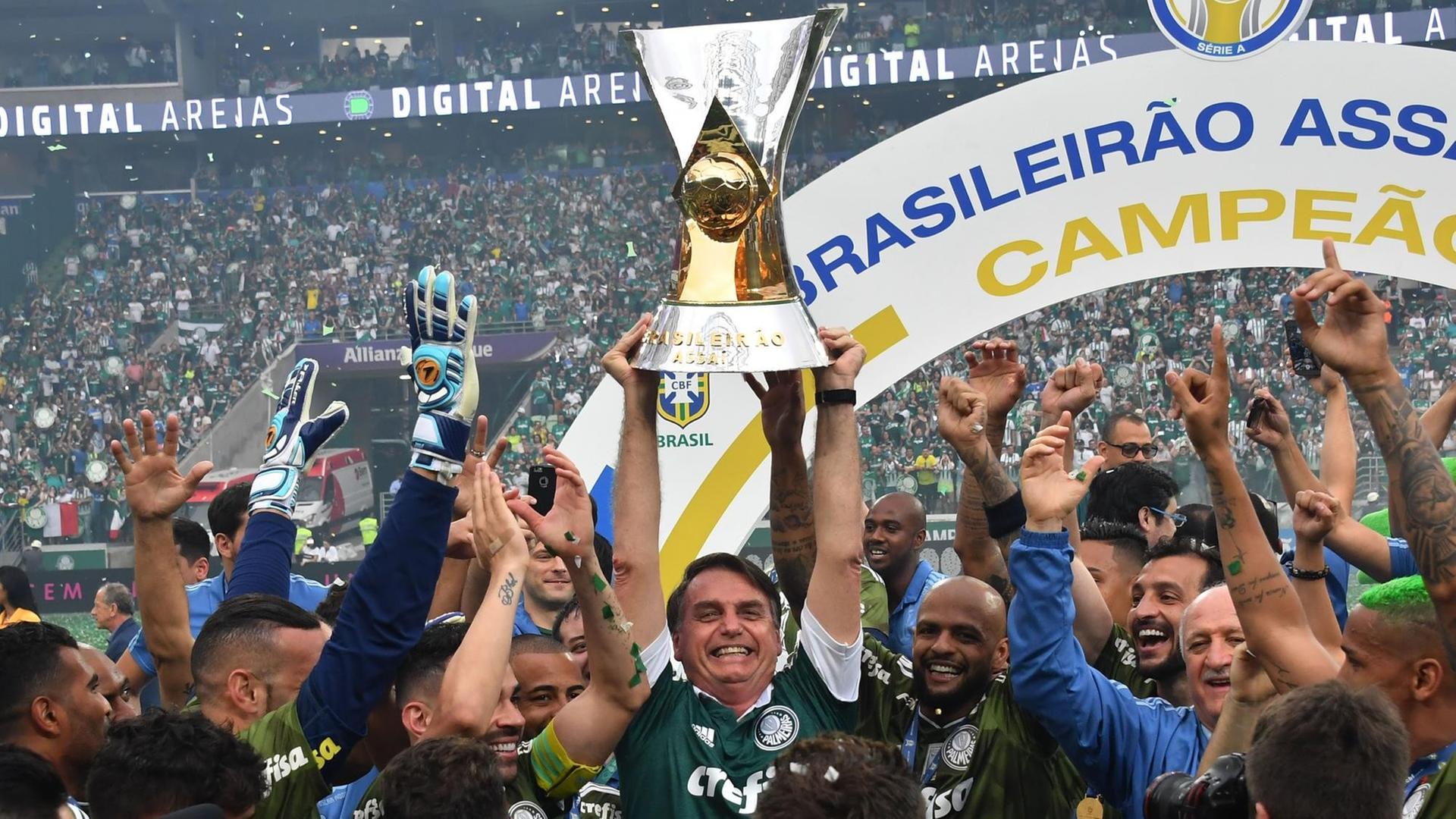 Brasiliens künftiger Präsident Jair Bolsonaro hebt den Pokal in die Luft, während er mit Palmeiras-Spieler den Titel feiert. Brasiliens künftiger Präsident Jair Bolsonaro hebt den Pokal in die Luft, während er mit Palmeiras-Spieler den Titel feiert.