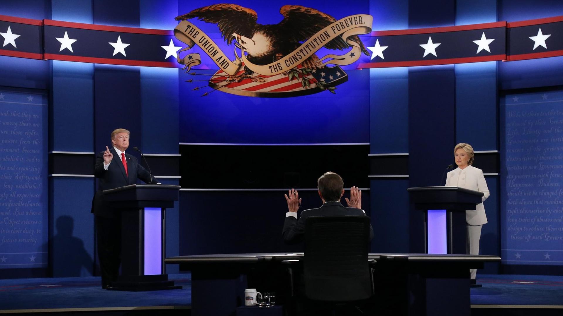 Auf der Bühne der letzten TV-Debatte stehen links der Republikaner Donald Trump und rechts Hillary Clinton. In der Mitte sitzt Moderator Chris Wallace mit dem Rücken zum Betrachter. Auf der Bühne der letzten TV-Debatte stehen links der Republikaner Donald Trump und rechts Hillary Clinton. In der Mitte sitzt Moderator Chris Wallace mit dem Rücken zum Betrachter.
