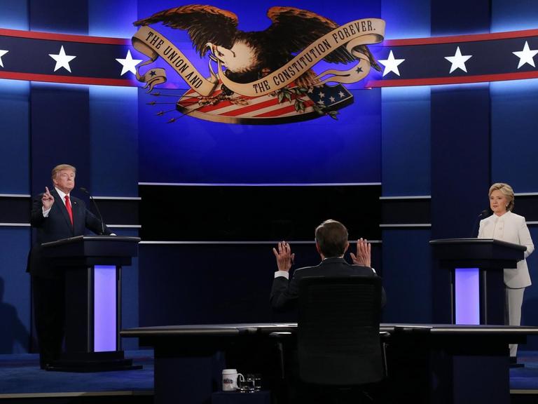 Auf der Bühne der letzten TV-Debatte stehen links der Republikaner Donald Trump und rechts Hillary Clinton. In der Mitte sitzt Moderator Chris Wallace mit dem Rücken zum Betrachter.
