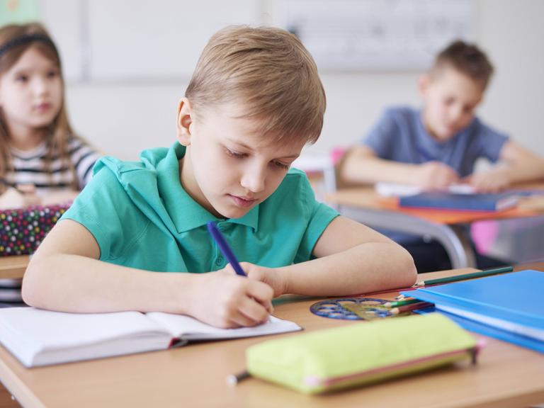 Schüler in einer Klasse, ein Schuljunge schreibt in ein Heft.