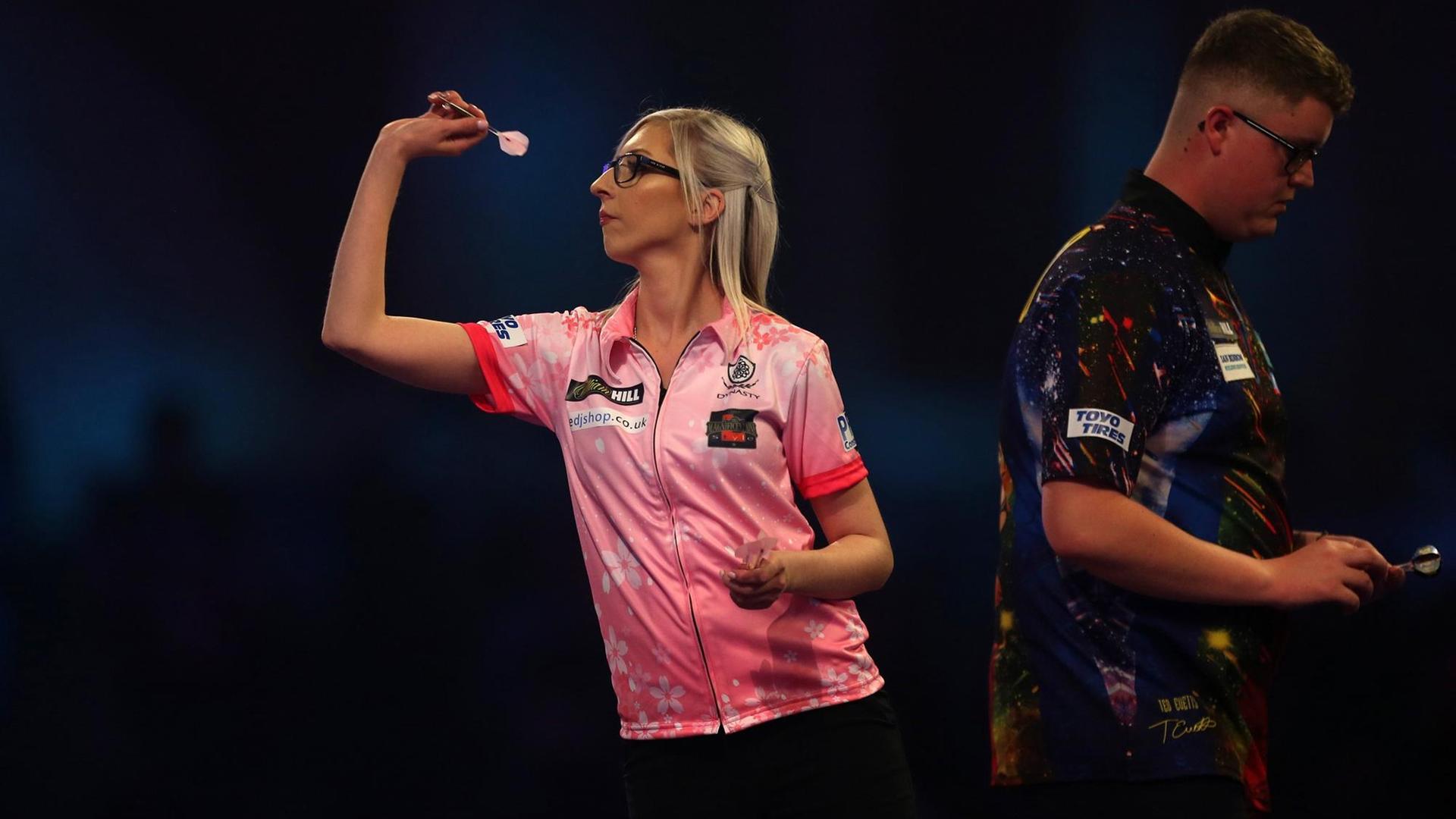 London: Darts: WM im Alexandra Palace. Fallon Sherrock hebt den Arm zum Abwurf eines Dart-Pfeils. Rechts im Hintergrund ihr Gegener Evetts. London: Darts: WM im Alexandra Palace. Fallon Sherrock hebt den Arm zum Abwurf eines Dart-Pfeils. Rechts im Hintergrund ihr Gegener Evetts.