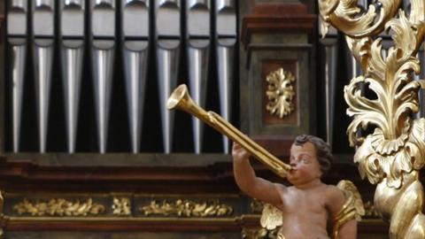 Eine große barocke Orgel ist mit einem Engel geschmückt, der vor den Pfeifen sitzt und eine Trompete spielt.