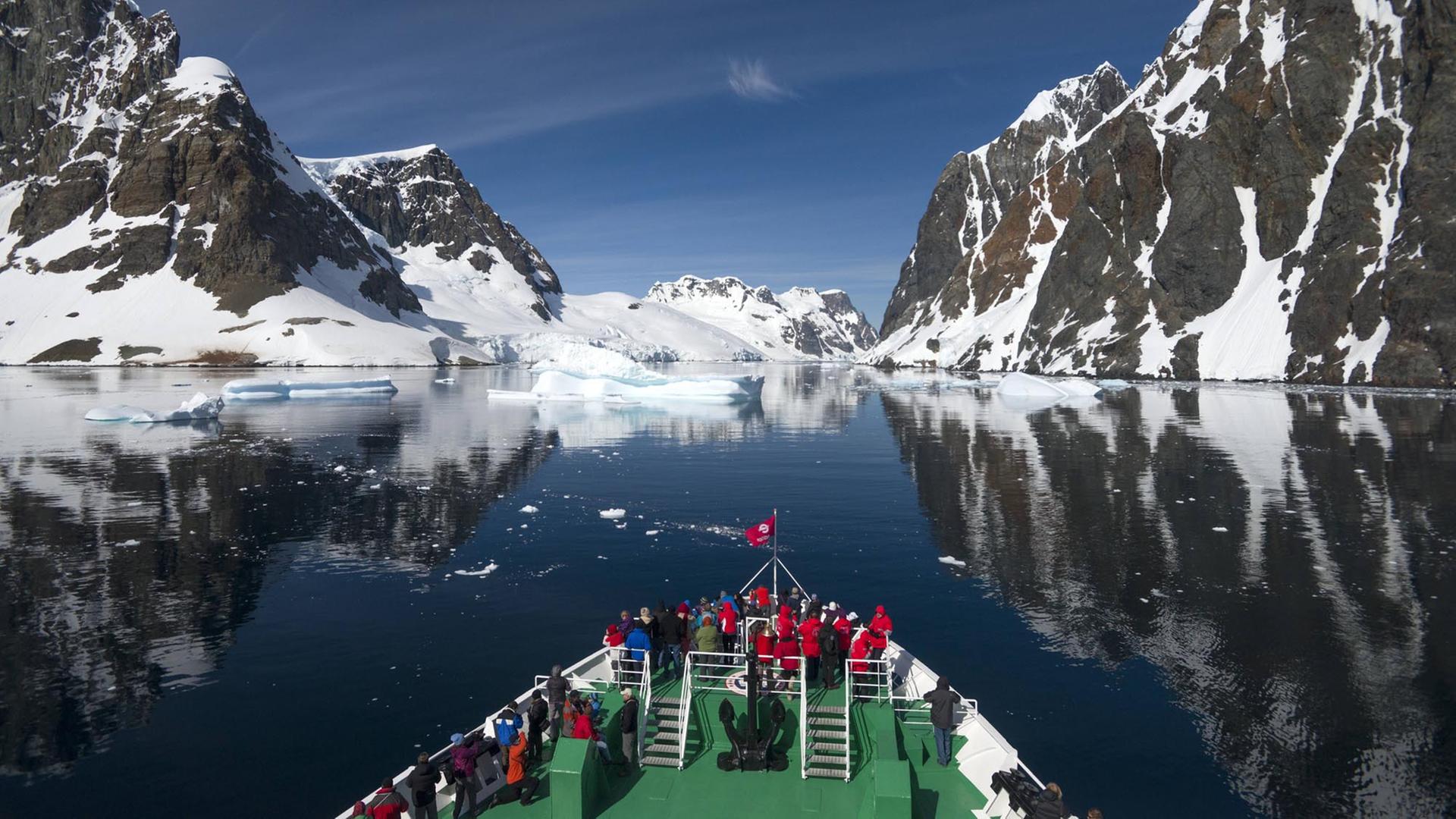 Besucher auf dem Bug des Expeditionskreuzfahrtschiffs MS Expedition betrachten sich spiegelnde Szenerie des Lemaire-Kanals auf der Antarktischen Halbinsel Besucher auf dem Bug des Expeditionskreuzfahrtschiffs MS Expedition betrachten sich spiegelnde Szenerie des Lemaire-Kanals auf der Antarktischen Halbinsel