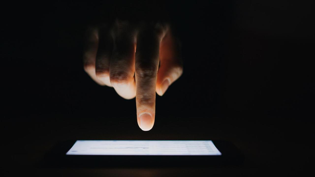 Eine Hand mit Zeigefinger tippt auf einen Bildschirm vor schwarzem Hintergrund. Eine Hand mit Zeigefinger tippt auf einen Bildschirm vor schwarzem Hintergrund.