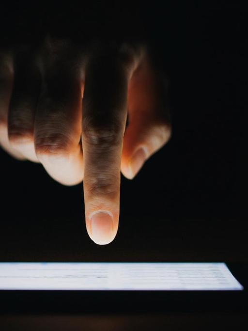 Eine Hand mit Zeigefinger tippt auf einen Bildschirm vor schwarzem Hintergrund.