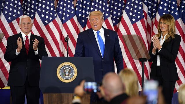 Donald Trump steht auf einer Rednerbühne. Rechts neben ihm Vize-Präsident Pence, links seine Frau Melania.