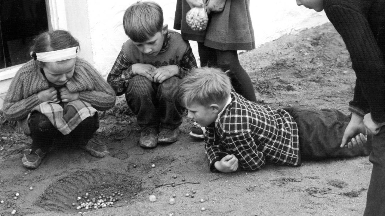 Fünf Kinder spielen im Sand mit Murmeln. Fünf Kinder spielen im Sand mit Murmeln.