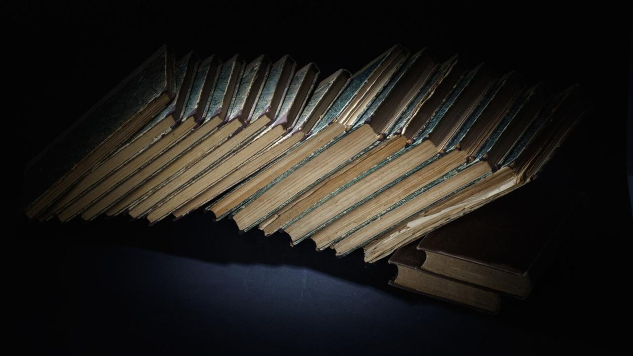 Mehrere alte Bücher liegen auf einer dunklen Unterlage. Mehrere alte Bücher liegen auf einer dunklen Unterlage.